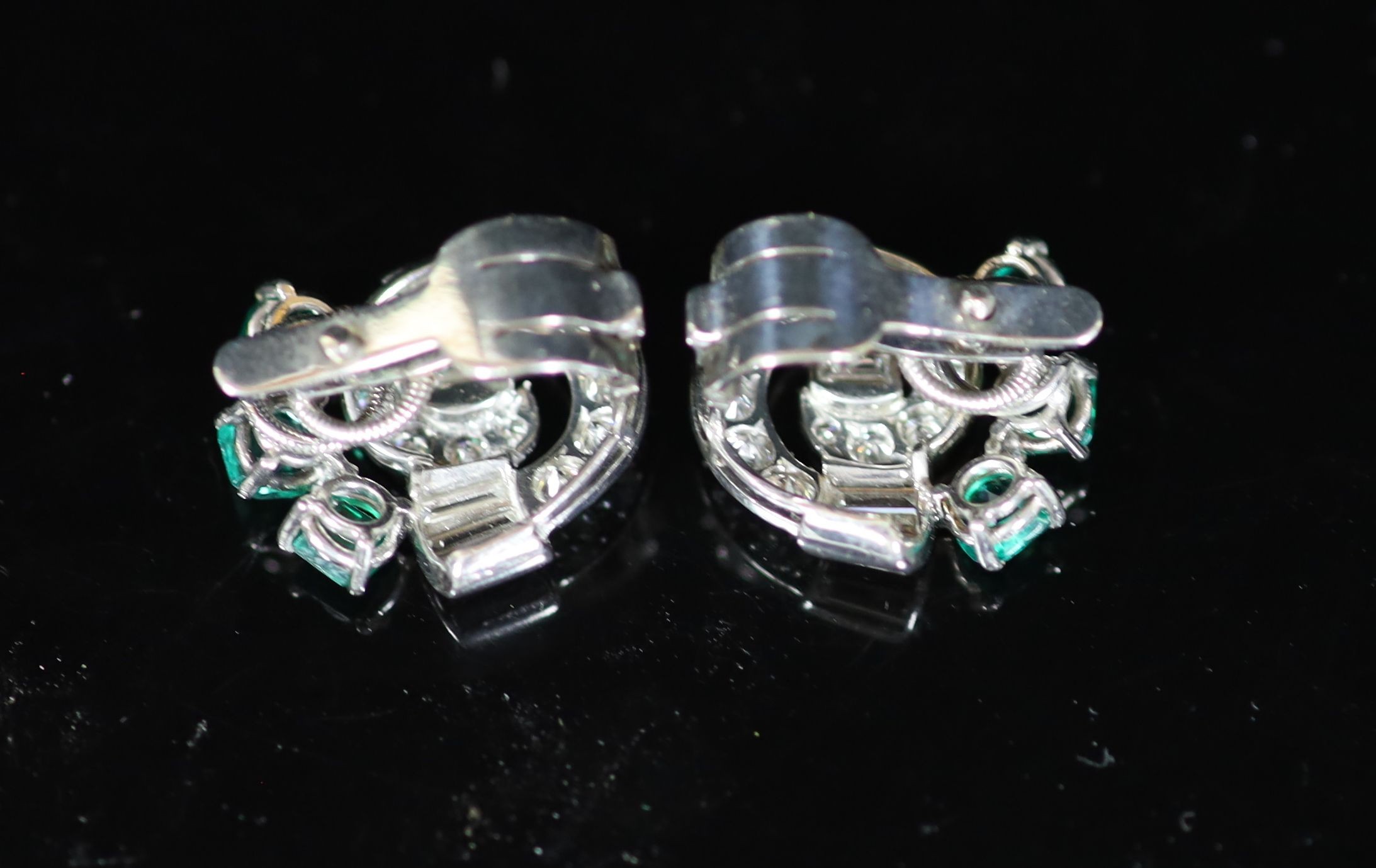 A pair of 1950's white gold, emerald and diamond cluster scroll ear clips